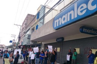 Pessoas em frente a loja Manlec segurando cartazes.