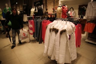 Interior de uma loja com diversas araras de roupas. Casacos pendurados.