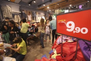 Pessoas comprando dentro de loja. Placa com fundo vermelho diz 9,90.