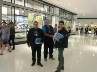 Três homens com planilhas na mão dentro de um shopping center.