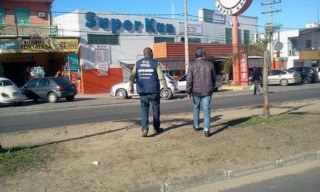 Dois homens de costas caminhando numa avenida. Ao fundo fachada do super Kan.