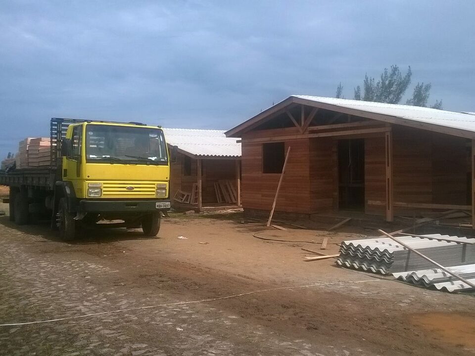 Terreno arborizado. Sob ele, três casas de madeira em fase final de construção.