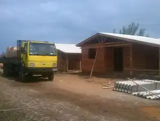 Terreno arborizado. Sob ele, três casas de madeira em fase final de construção.