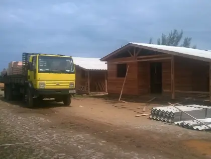 Terreno arborizado. Sob ele, três casas de madeira em fase final de construção.