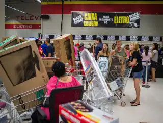 Pessoas na fila do caixa de um aloja, com carrinhos carregados com caixas de televisão de plasma.