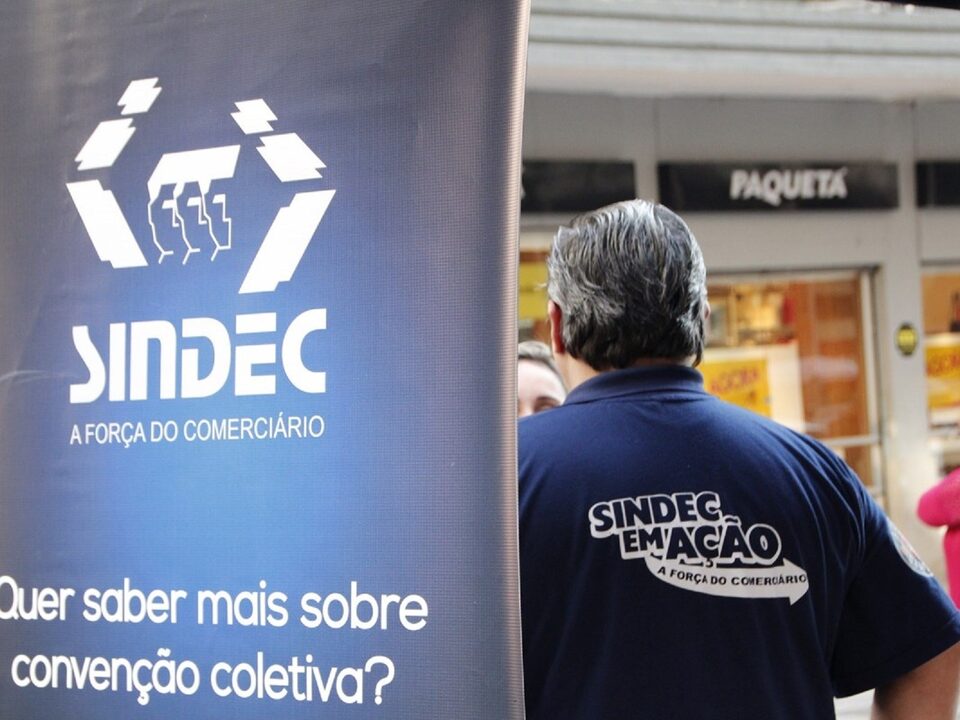 Banner com o dizer: Quer saber mais sobre convenção coletiva?. Ao fundo homem de costas com uma camiseta escrito Sindec em Ação