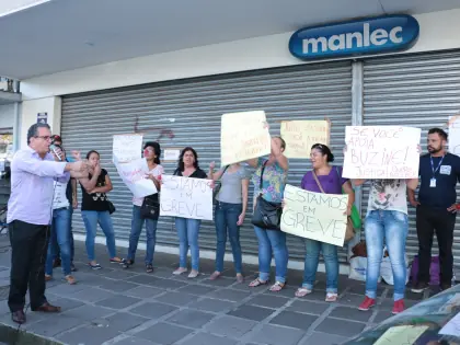 Mulher com nariz de palhaço falando no microfone. Atrás dois cartazes. Um diz: Não aguento mais, 5 meses sem salário. O outro: Justiça!