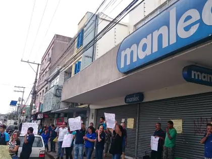 Pessoas em frente a loja Manlec segurando cartazes.