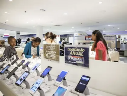 Celulares em uma prateleira. Pessoas olhando.