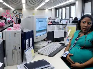 Mulher grávida sentada em um escritório. Sob a mesa computador e papéis.