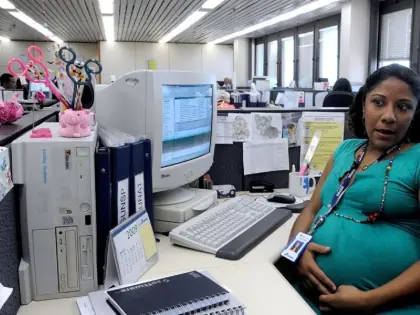 Mulher grávida sentada em um escritório. Sob a mesa computador e papéis.