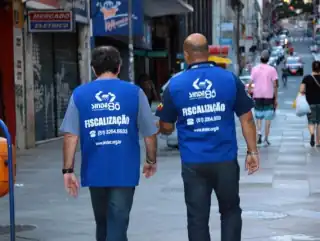 Dois homens de costas caminhando na rua. No colete que eles usam diz, fiscalização.