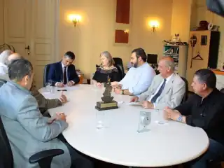 Pessoas sentadas no entrono de uma mesa. Homem do centro assina um documento.