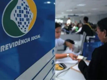 Placa escrito previdência social. Ao fundo mulher sendo atendida.