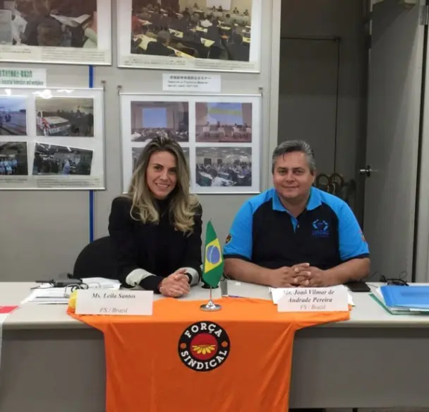 Mulher e homem sentados. Na mesa uma camiseta com a logo da força Sindical