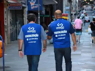 Dois homens de costas caminhando. No colete tem o dizer 