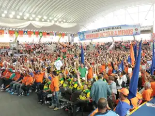 Ginásio com muitas pessoas sentadas e com bandeiras