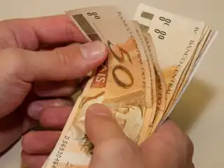 Mão pegando notas de 50 reais.