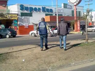 Dois homens de costas caminhando numa avenida. Ao fundo fachada do super Kan.