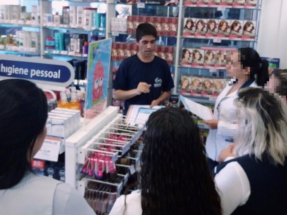 Dentro de uma farmácia, homem fala e cinco mulheres prestam atenção.